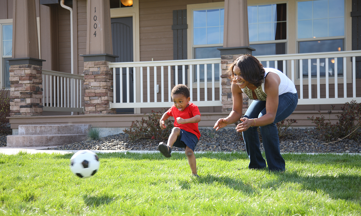 Boy and woman playing soccer in front of house