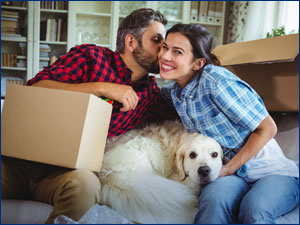 man woman and dog sitting on couch with boxes surrounding them