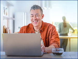 man sitting at table looking at laptop screen