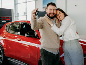 man and woman taking selfie in front of red car