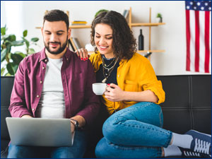 man and woman sitting on couch viewing the laptop screen