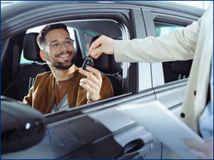 salesperson handing over car key through window to man sitting in car