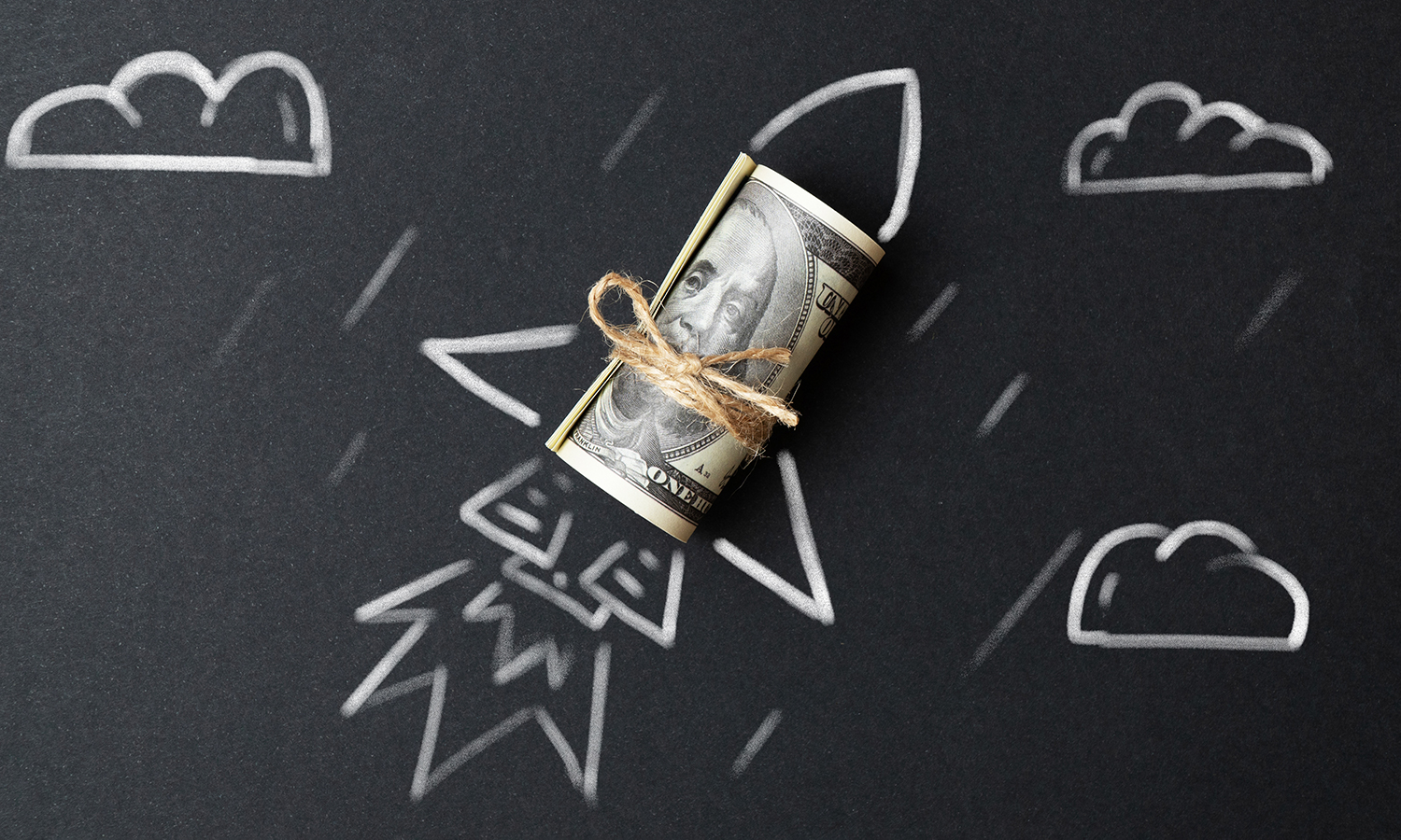 Roll of money with rocket scene drawn around it on a chalkboard