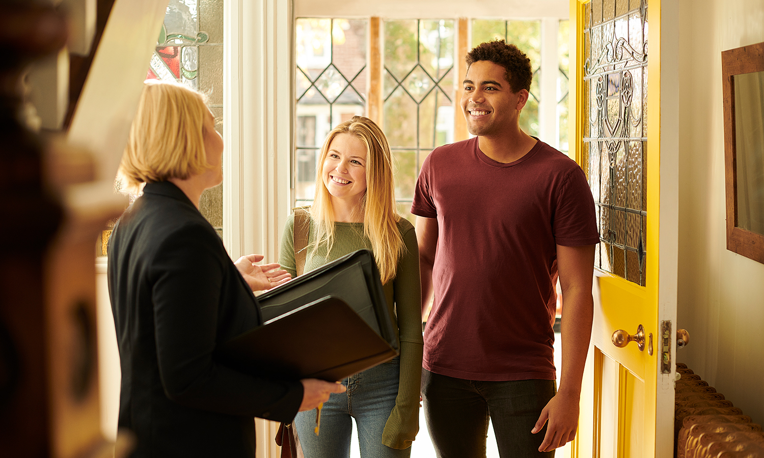 Young woman and man talking to real estate agent while visiting house