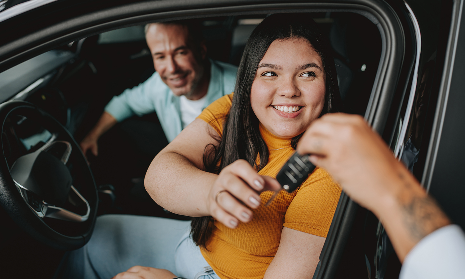 Teenage girl getting keys to drive a car while dad sits in passenger seat