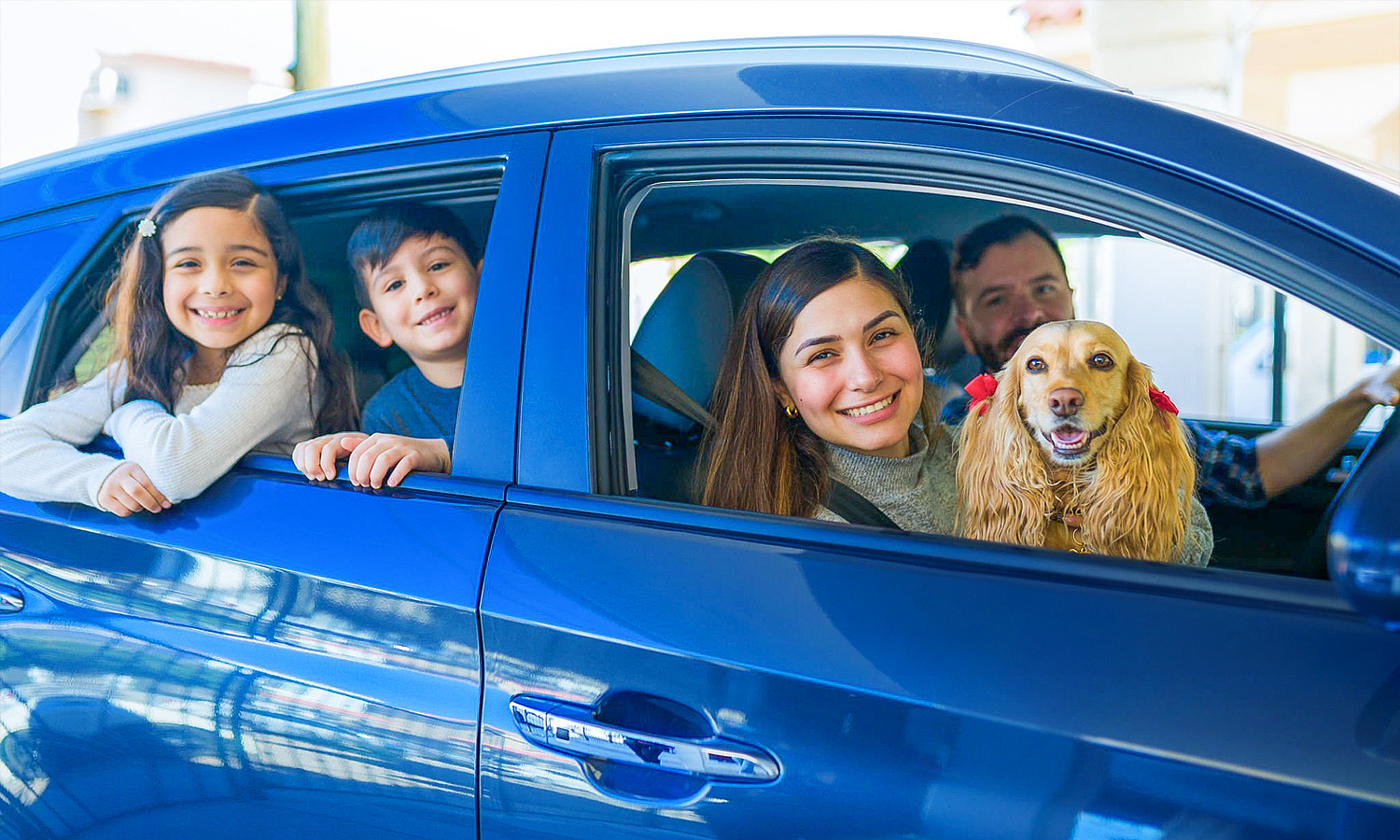 man, woman, children and dog looking out the passenger windows of a blue car