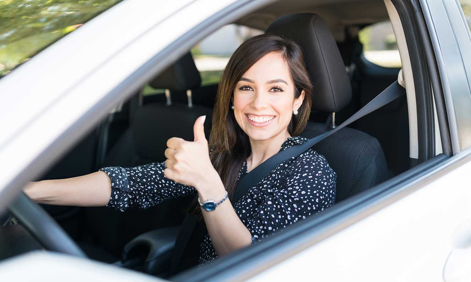 woman sitting in drivers seat of car looking out the window with a thumbs up