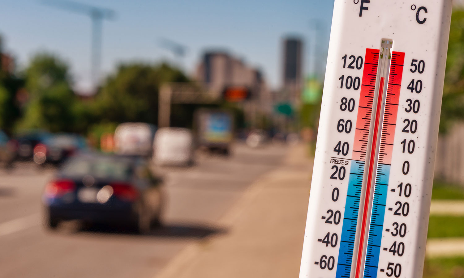 thermometer showing over 100 degrees Fahrenheit in front of a blurred out cityscape