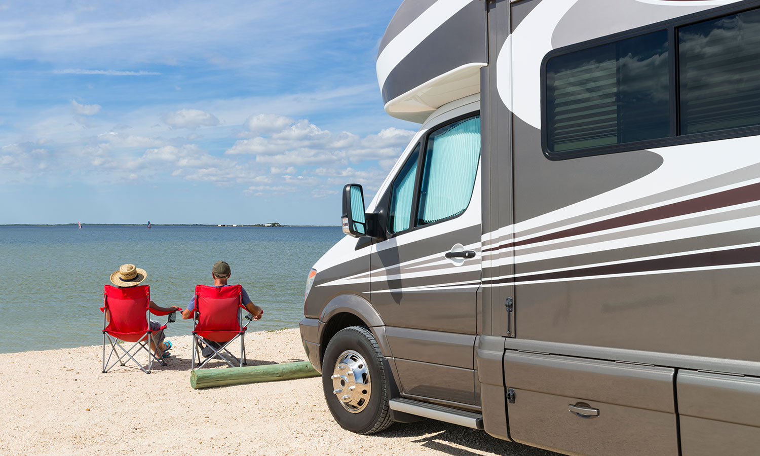 two people sitting on the beach in foldable chairs in front of an RV