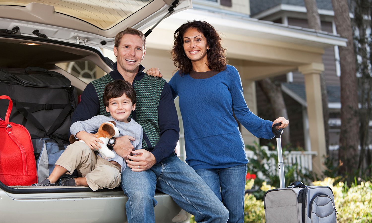 man woman and child sitting in trunk of suv in front of their home with suitcases