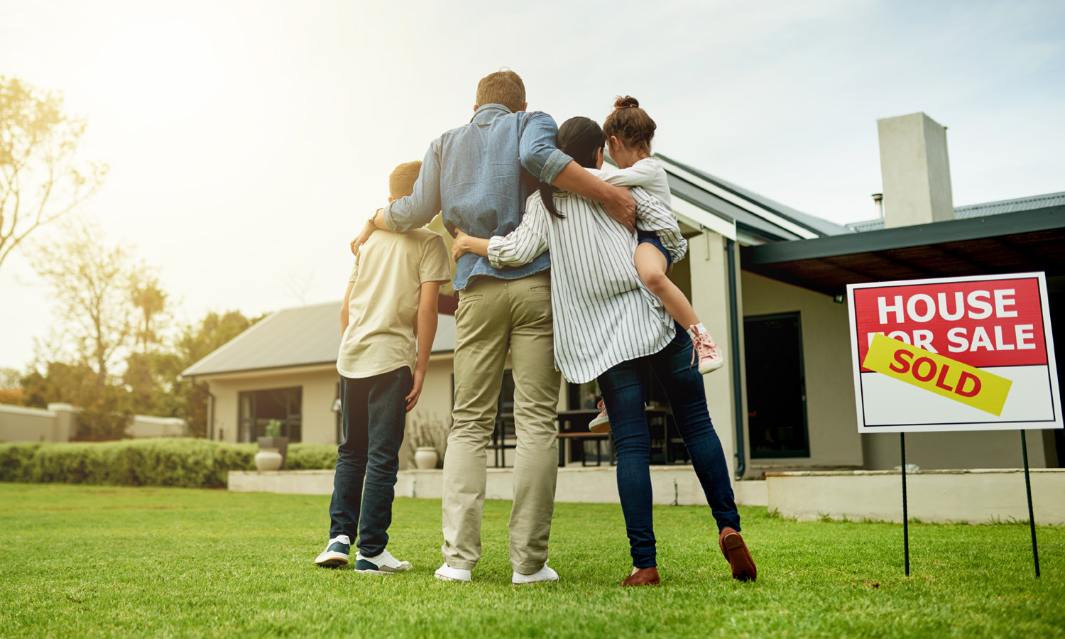 family hugging in the front yard facing a home with a sold sign