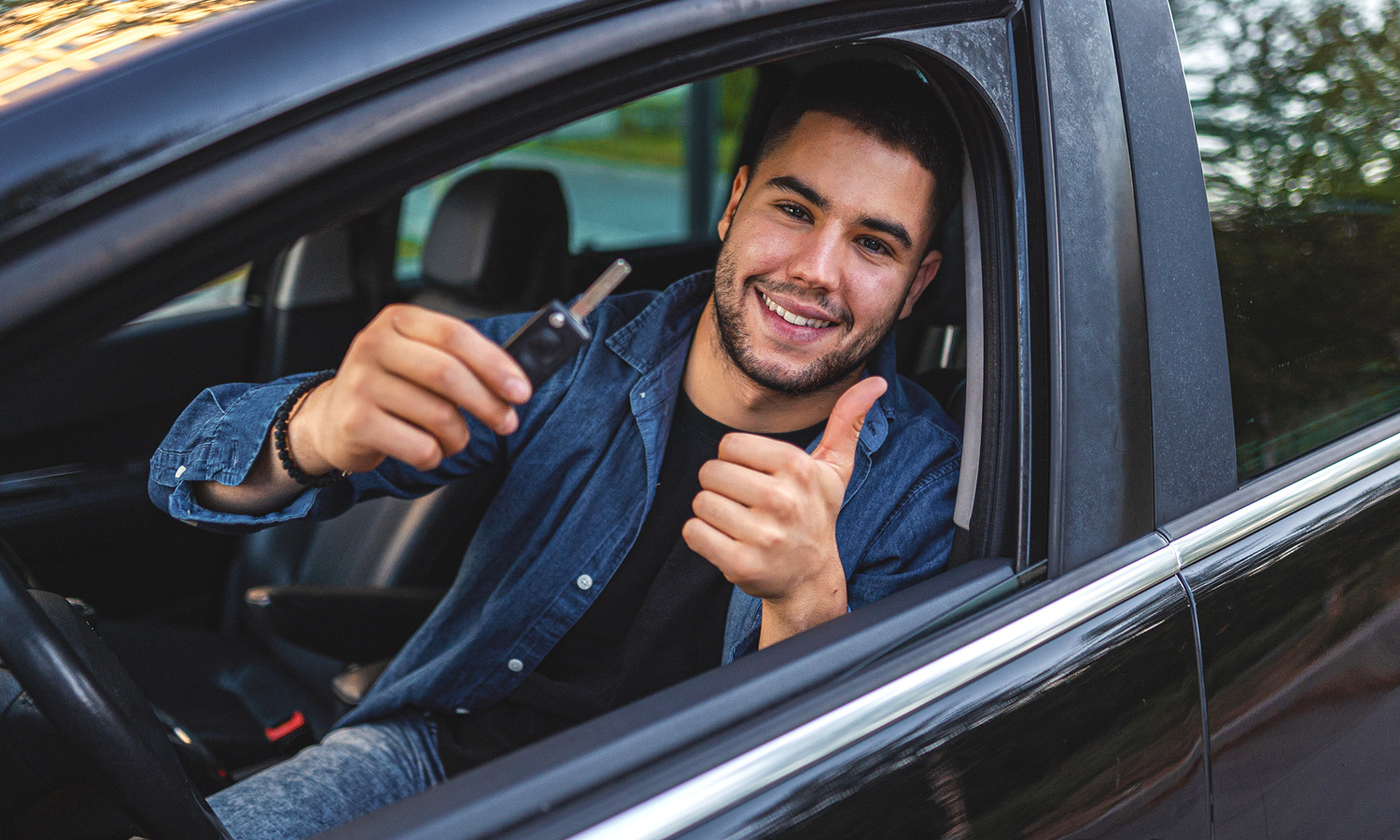 man sitting in driver seat looking out the window holding a key with a thumbs up