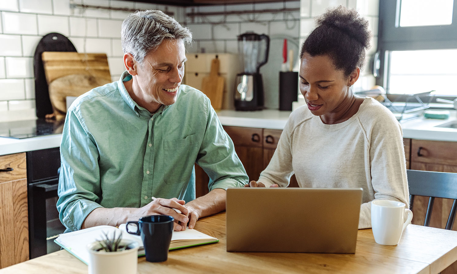 man and woman sitting at table in the kitchen looking at laptop and writing notes