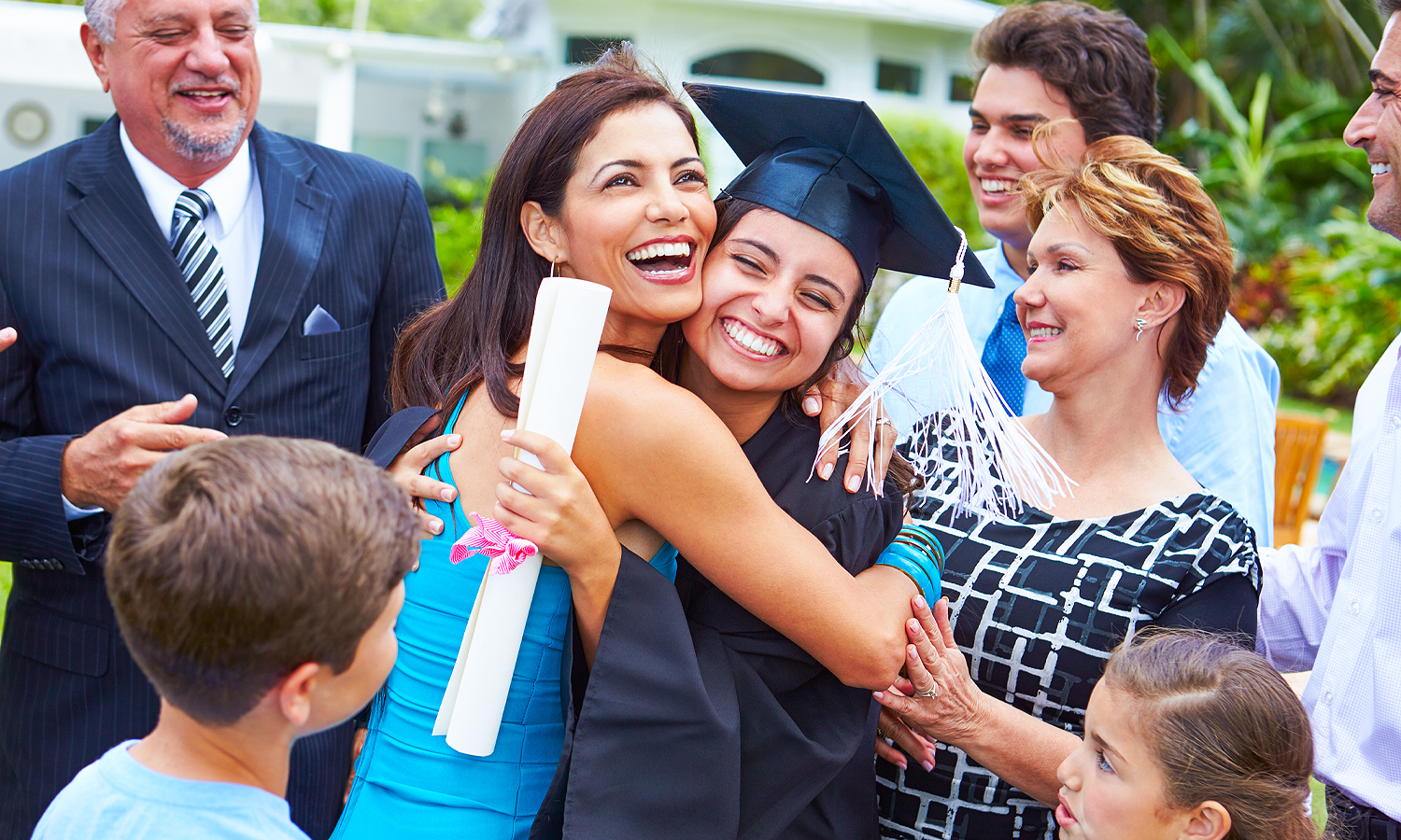 woman in graduation cap and gown holding a diploma smiling and surrounded by people