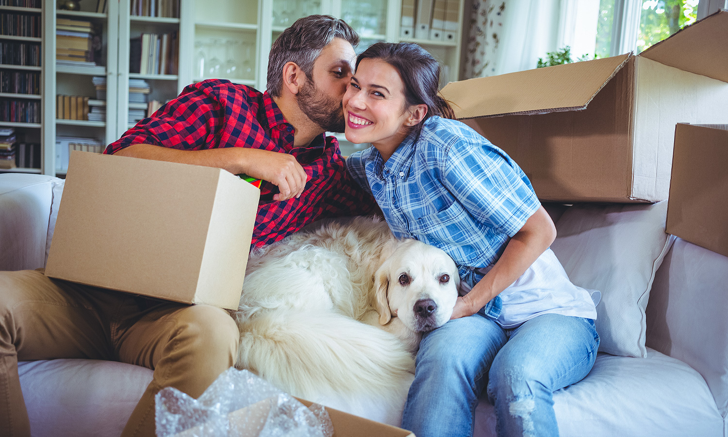man woman and dog sitting on couch with boxes surrounding them