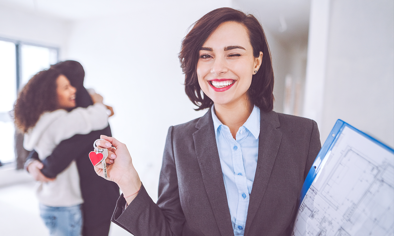 Couple hugging behind a real estate agent with keys in her hand.