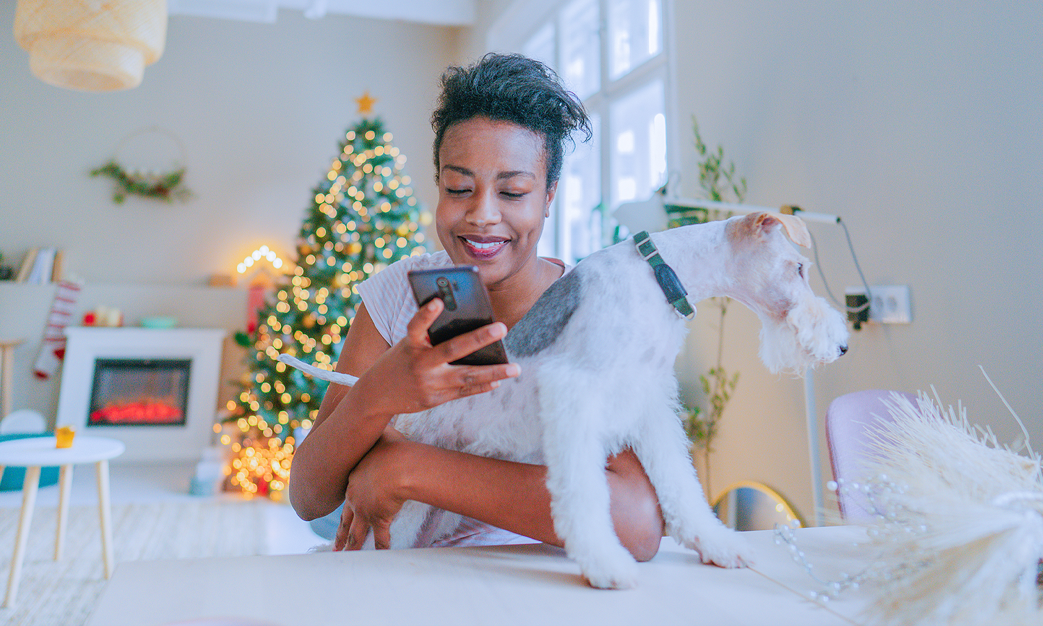 woman holding dog and looking at mobile phone with Christmas tree in the background