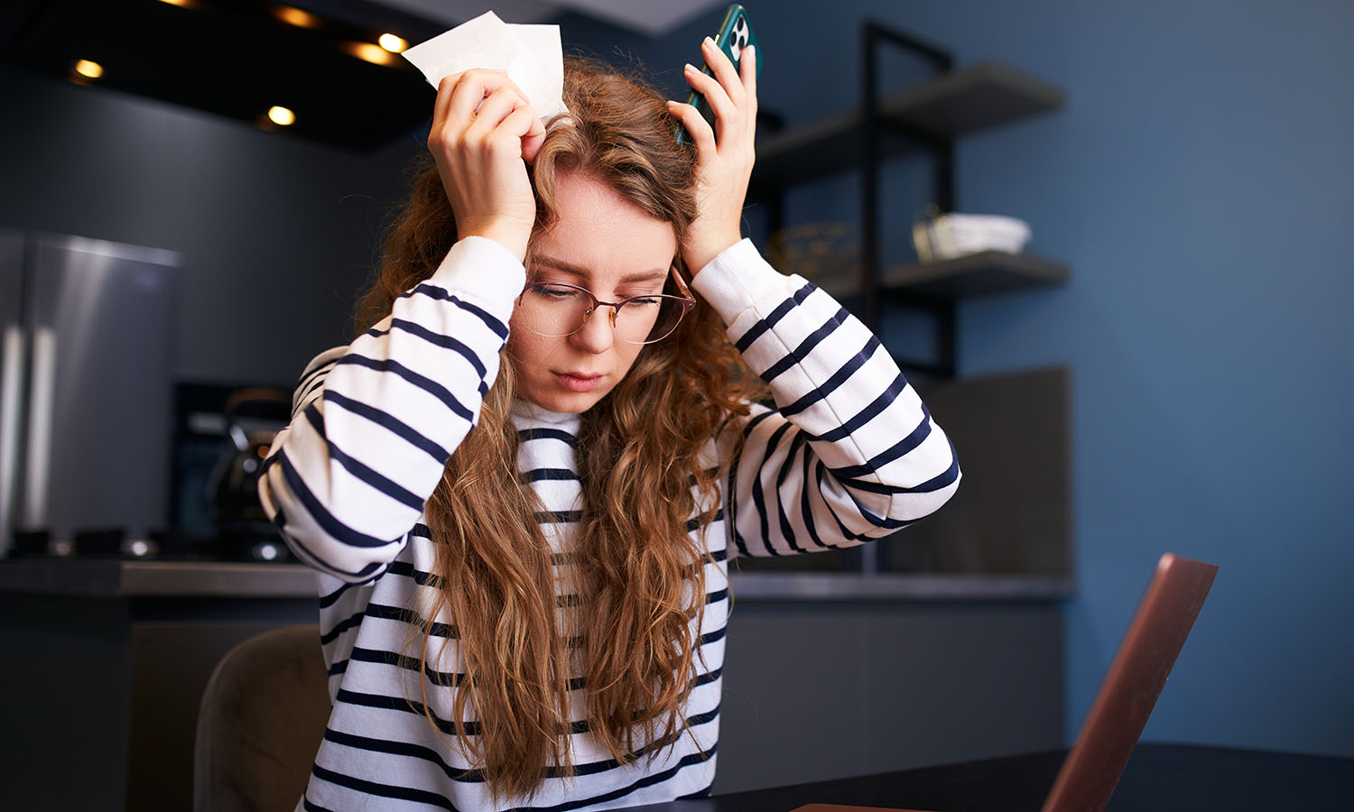 woman holding head sitting in front of laptop