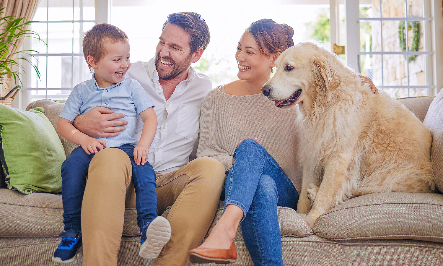 toddler, man, woman and dog smiling while sitting on couch
